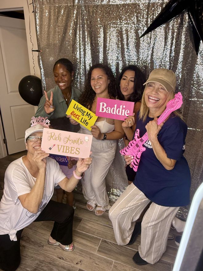 Guests posing with signs and a pink guitar prop in front of the silver sequin backdrop